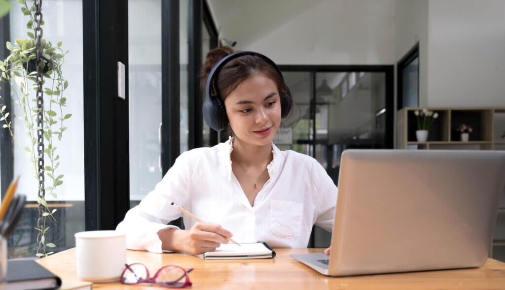 Asiatische Dolmetscherin verfasst Übersetzungen aus einer Fremdsprache ins Englische und hört dabei einen Audioaufnahme durch ihren Kopfhörer ab