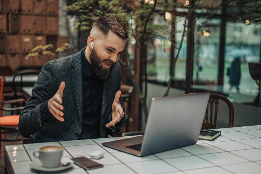 Young handsome businessman using laptop for an online meeting with his colleagues while working from a cafe