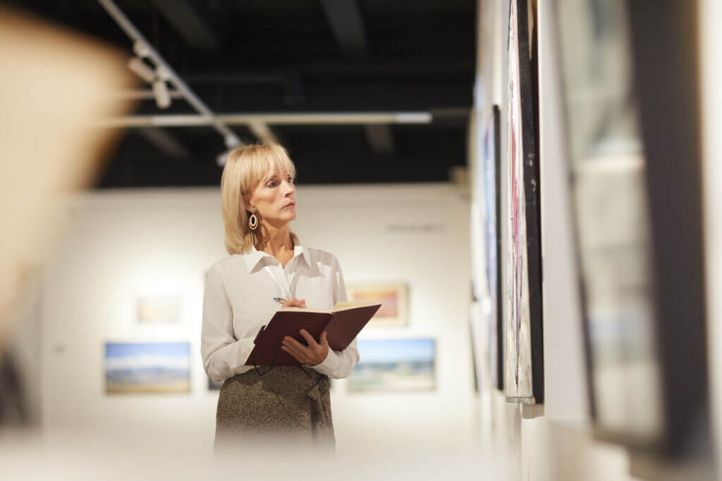 Waist up portrait of elegant mature woman looking at paintings in art gallery hall and enjoying museum exhibition, copy space